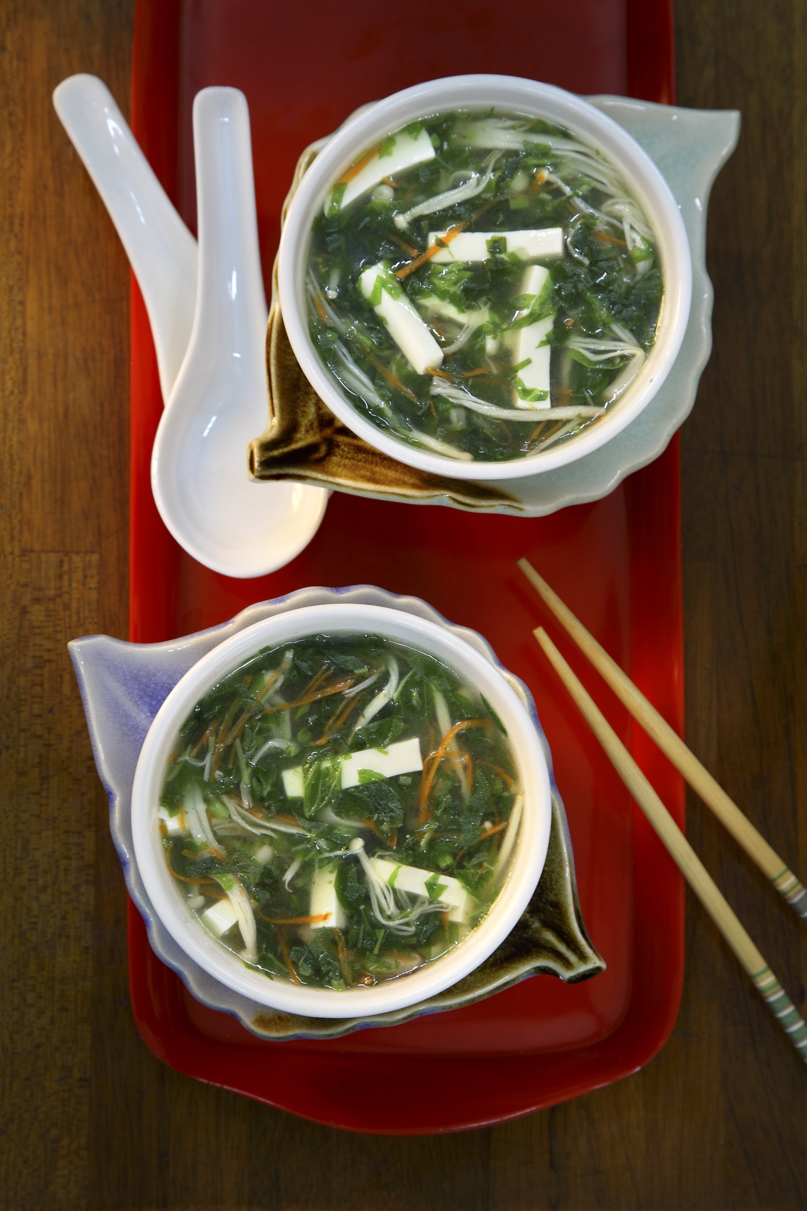 Two bowls of clear soup with greens and herbs